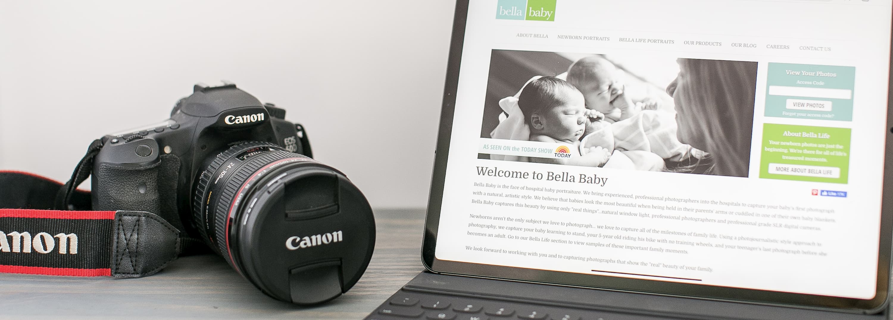 A professional camera sitting to the left of a laptop showing Bella-Baby's website