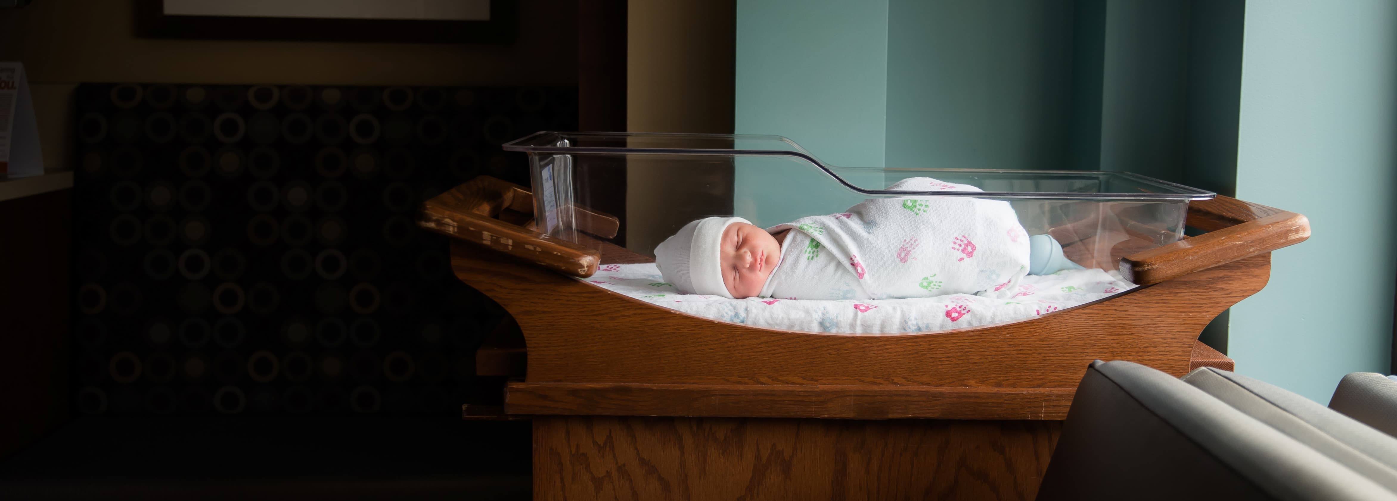 A blanket wrapped baby looking up with a brown bow on their head and text to view our work